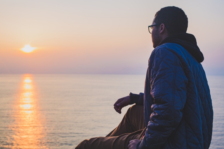 A man sitting by a body of water looking at the sunset.