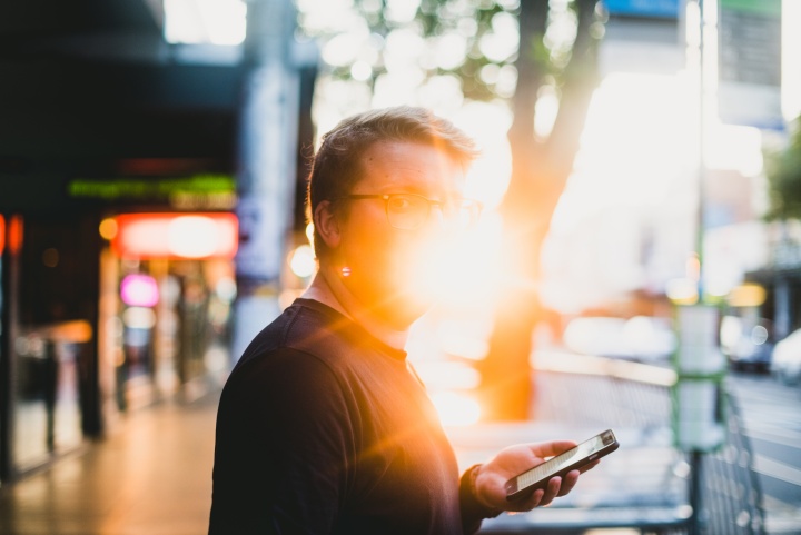A man holding a smartphone with the sun glaring behind him.