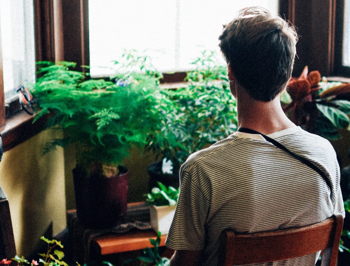 A young man sitting in a chair looking out a window.