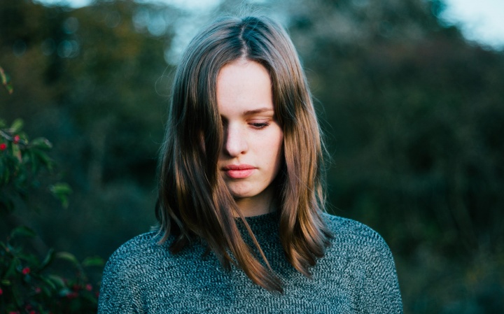 A young woman holding her head down facing the ground.