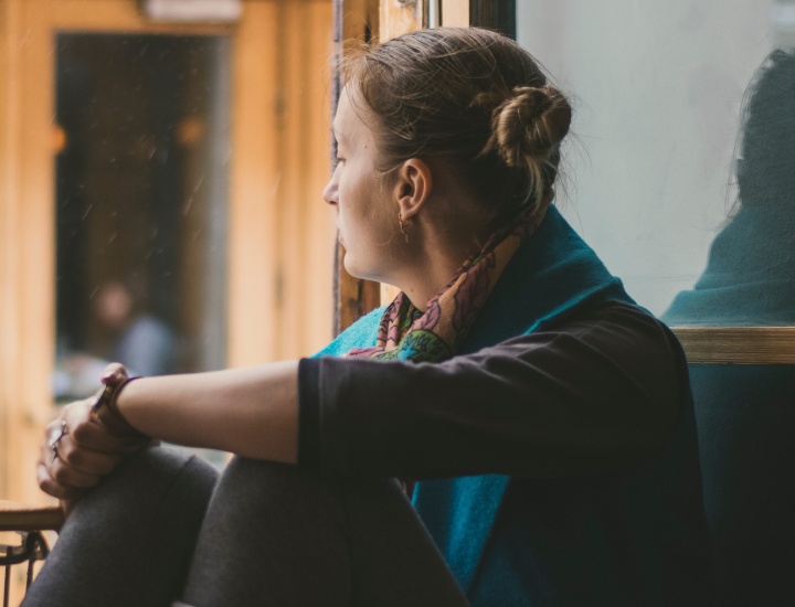 A woman sitting by a large window looking outside.