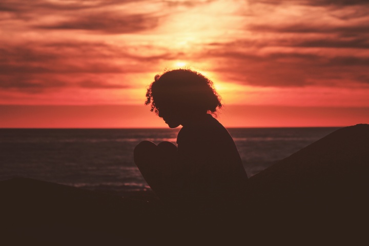 A silhouette of young woman with the sun setting in the background.