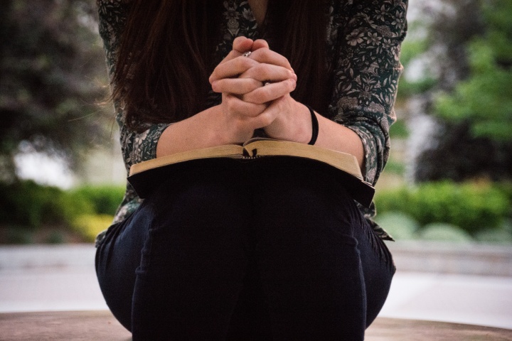 A woman with her clasped in prayer on top of an open Bible.