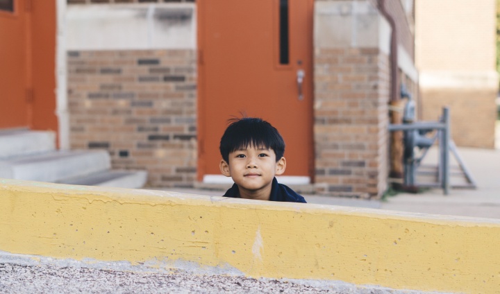 A little boy hiding behind a yellow wall.