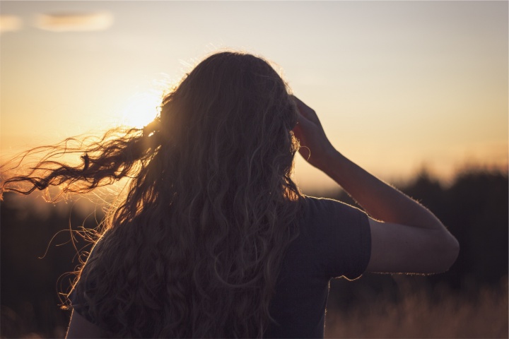 A young woman looking at the setting sun.