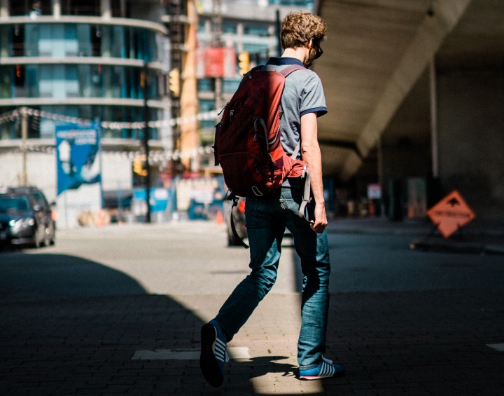 A man writing on the street wearing a backpack.