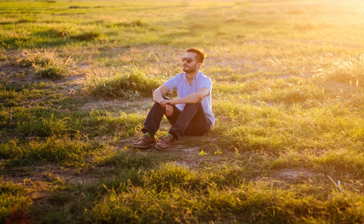 A man sitting in a field with the sun rays shinning.
