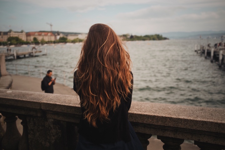 A woman standing on a bridge and looking out over the water.