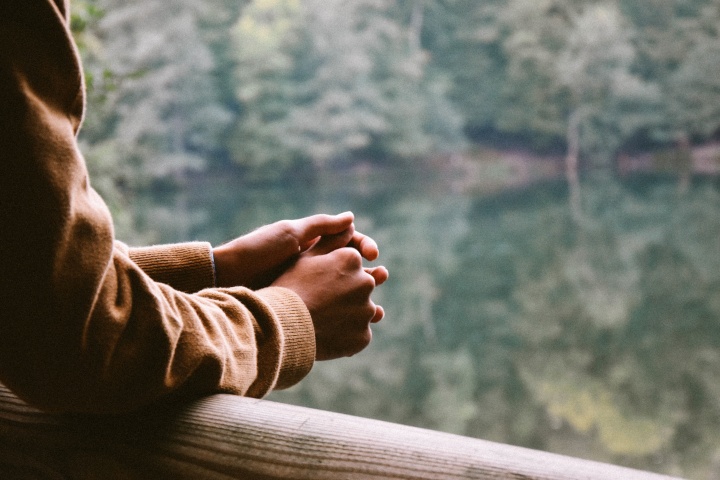 A person resting their arms on rail while looking out over a body of water.