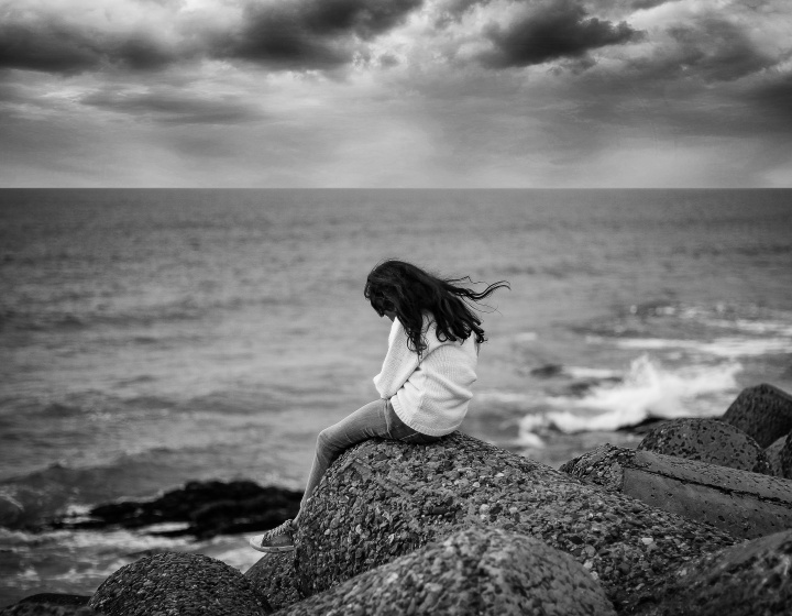 A woman sitting on a rock next to large body of water.