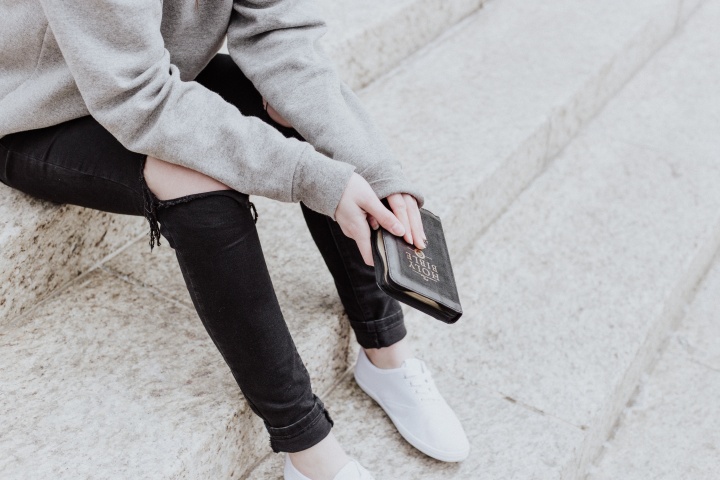 A woman sitting on concrete steps holding a Bible.