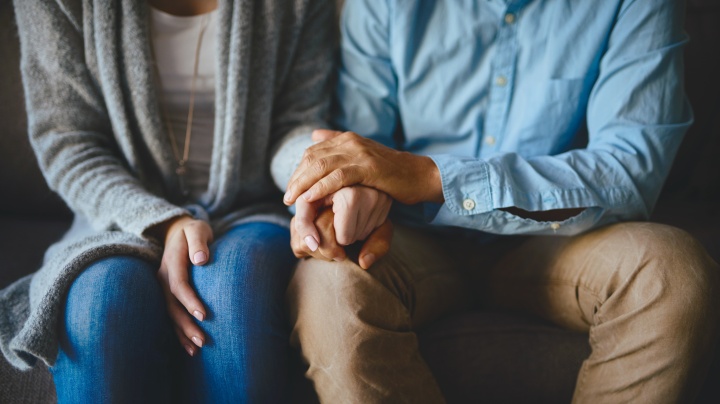 A husband and wife sitting down holding hands.