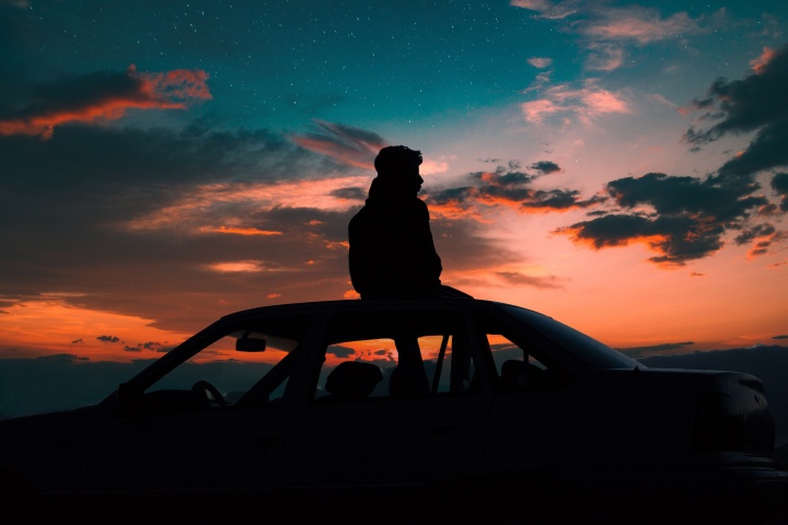 A young man sitting on the top of a car watching the sunset.