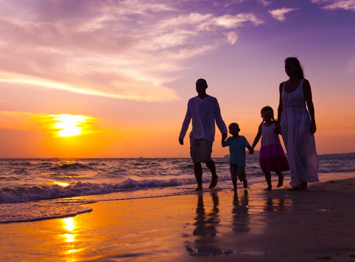 A family of four walking on the beach at sunset.