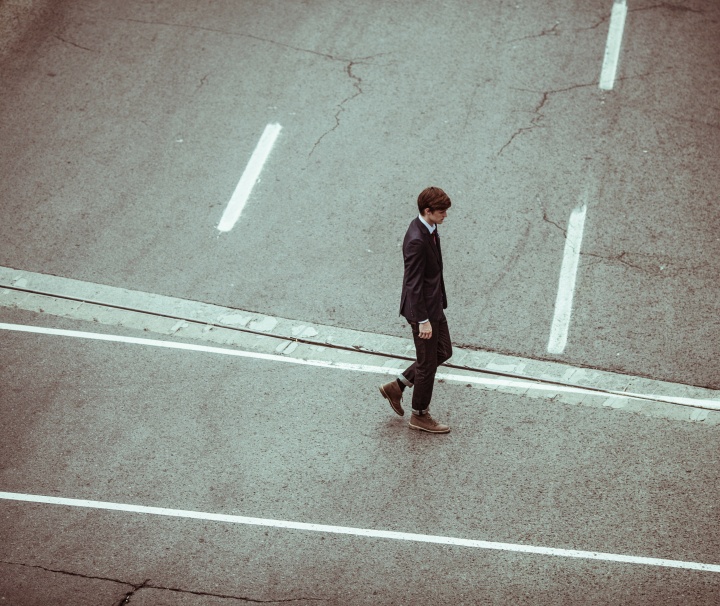 A young man in a suit walking across a road.