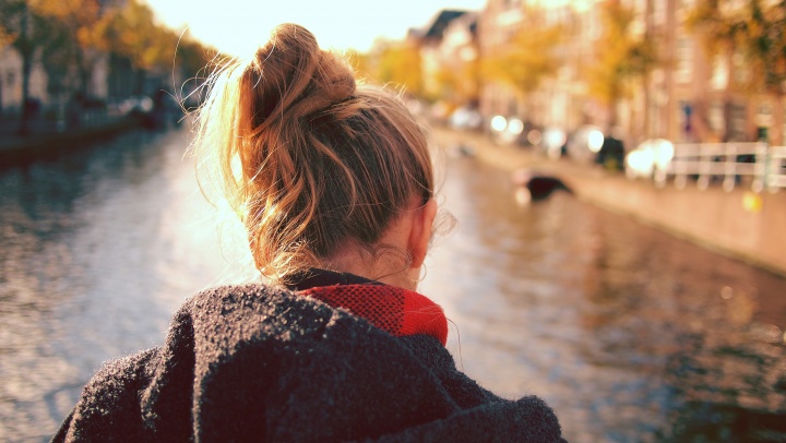 A woman looking down at water that is flowing past a bridge.