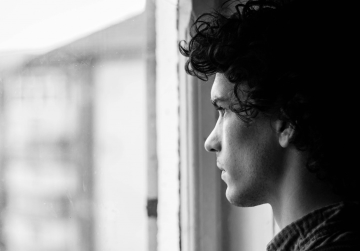 A young man with dark hair staring out a window.