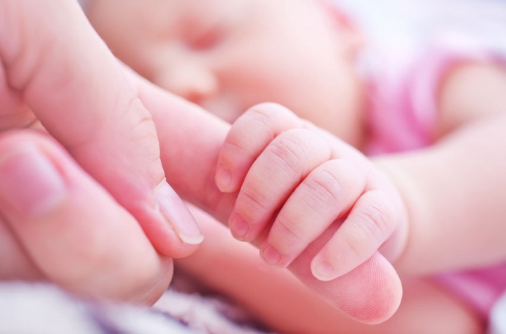 A baby holding the fingers of their mother.