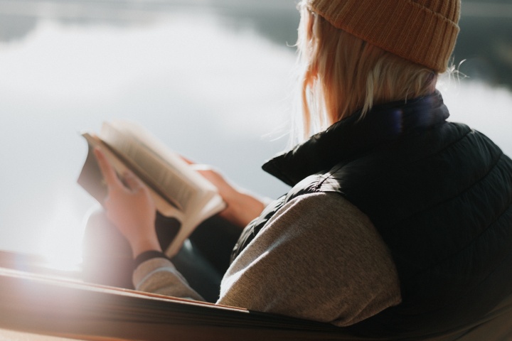 A woman sitting by a lake paging through a Bible.