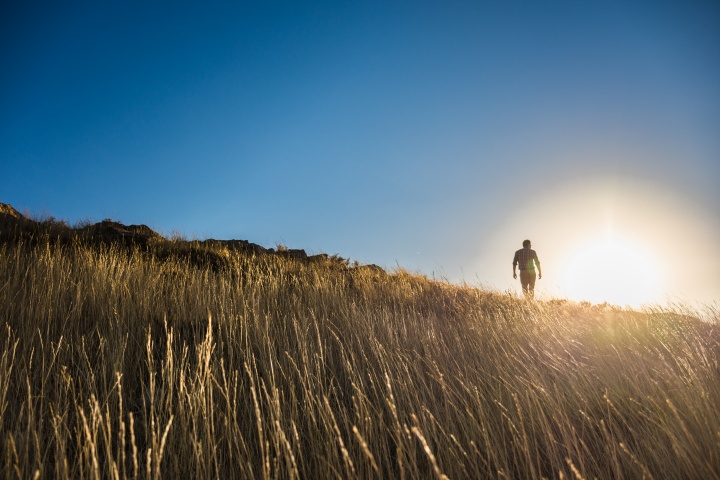A man walking up a grassy hill with the bright sun in the background.