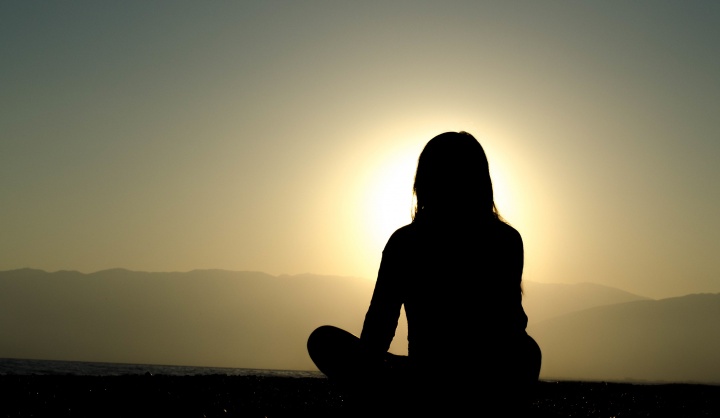 A woman sitting on the ground watch the setting sun.