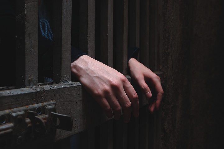 A person behind cell bars of a prison door.