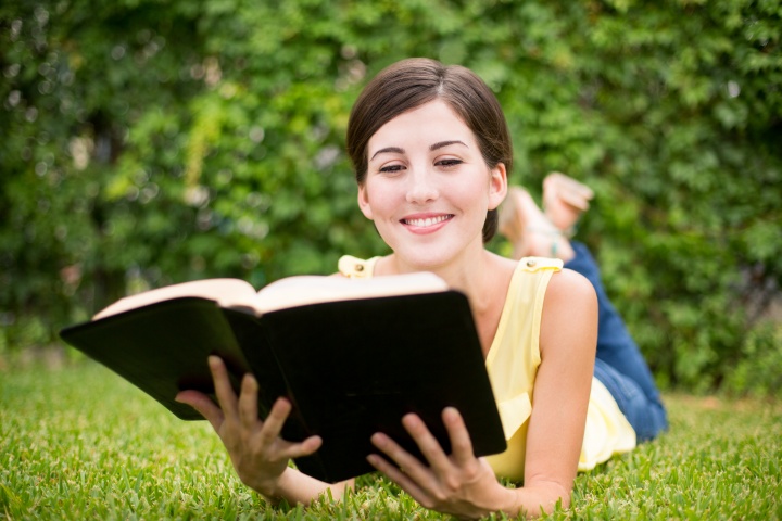 A woman reading a Bible while laying on a grassy field.