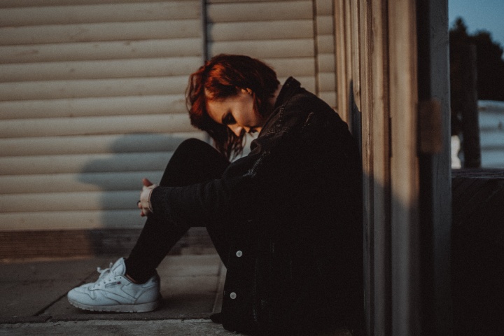 A young woman sitting on the ground hunched over as if she is struggling in life.