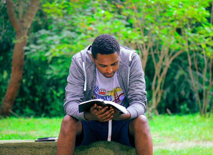 A man sitting on a bench reading a Bible.