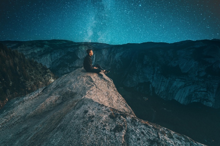A young man sitting on a rock looking at the night sky.