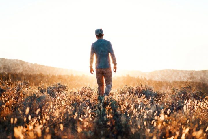 A man walking in a field with the sun rays shining on him.