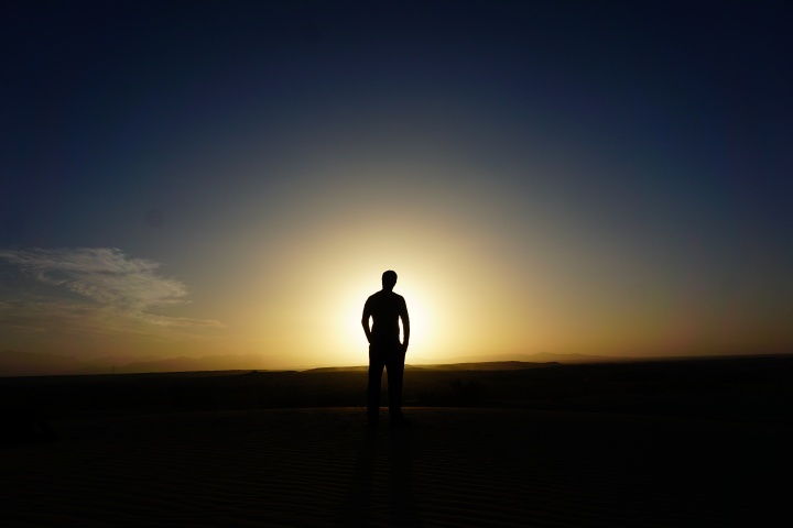 A man walking in a field with the sun rays shining on him.