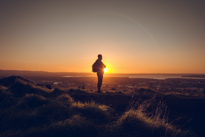A man standing on a hill with the sun setting.
