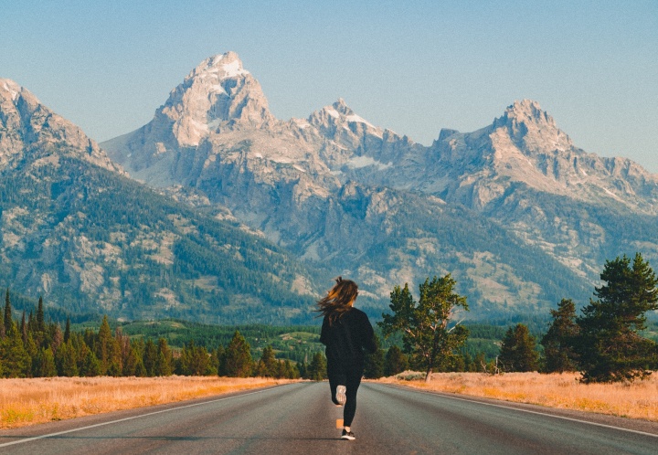 Photo of a person running towards mountains in the middle of an empty road.