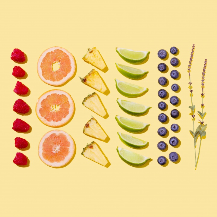 Rows of fruit aligned geometrically including pineapples, blueberries, raspberries and limes