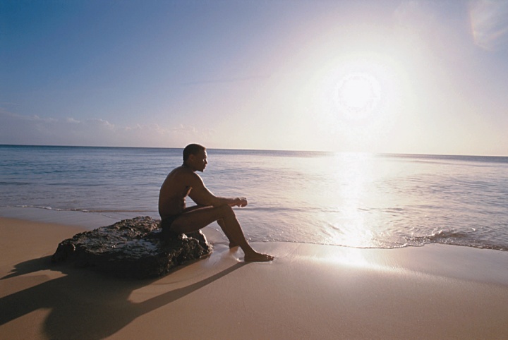 A man sitting on a rock on the beach.