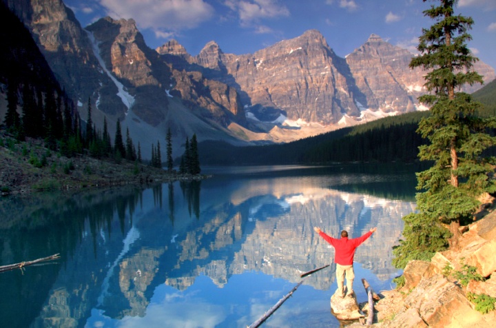 A man standing by a lake in the mountains.