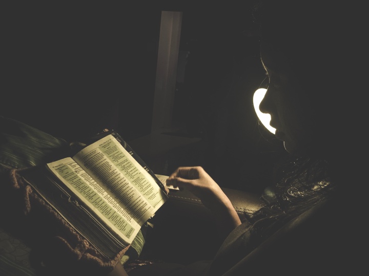 A person reading a Bible by a lamp.