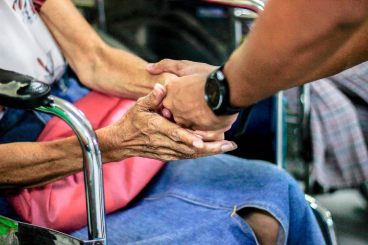 Photo of a younger person's hands gently holding an older person's hands on a subway.