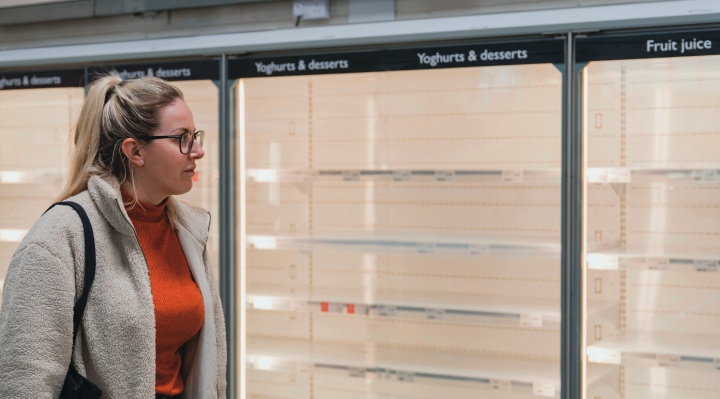 A woman looking at empty shelves inside a grocery store.