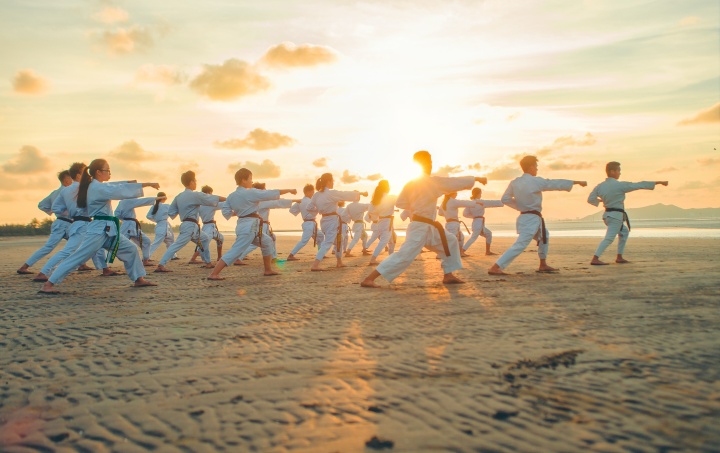 A group of people practicing martial arts moves on a beach.