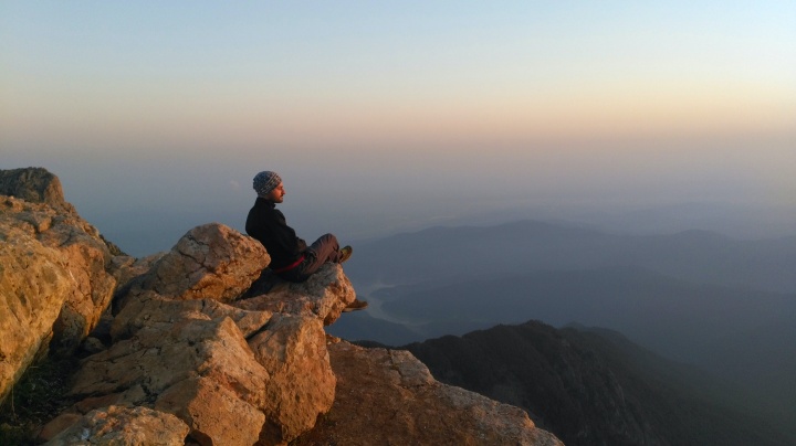 A person sitting on large rocks looking out over a cliff.