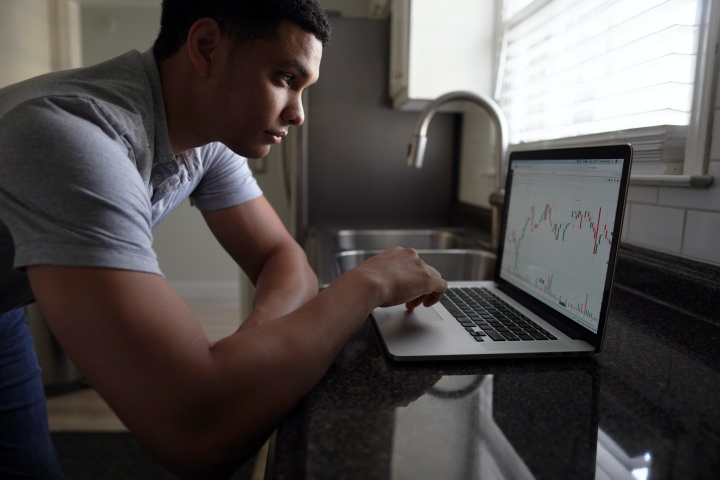 A young man looking at his laptop displaying a graph.