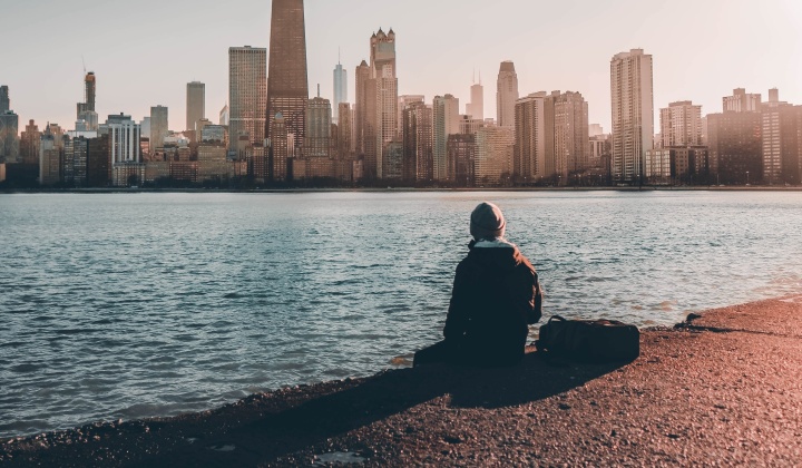 A person sitting at the edge of water looking at a city skyline.