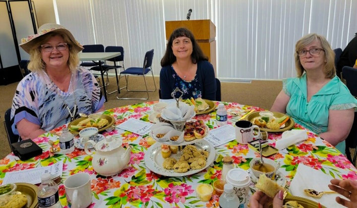 three ladies seated at a table enjoying tea and desserts