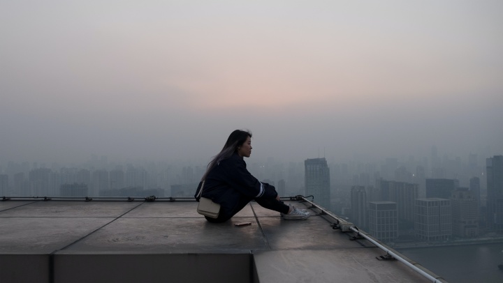 A woman sitting on a rooftop looking out.