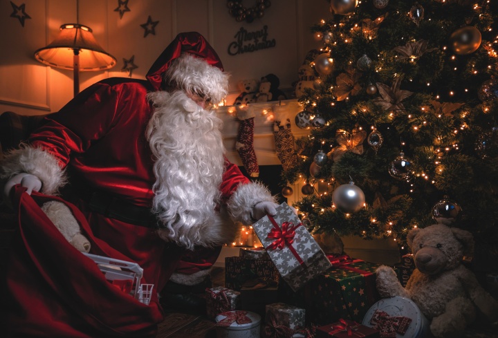 Santa Claus putting gifts under a Christmas tree.
