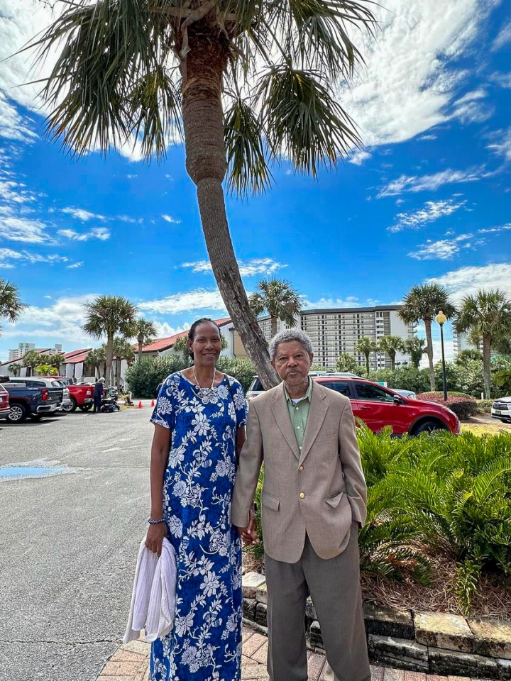 a couple standing outdoors in front of a palm tree