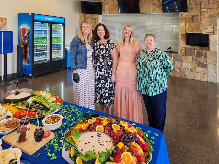 four ladies gathered by a table of colorful food