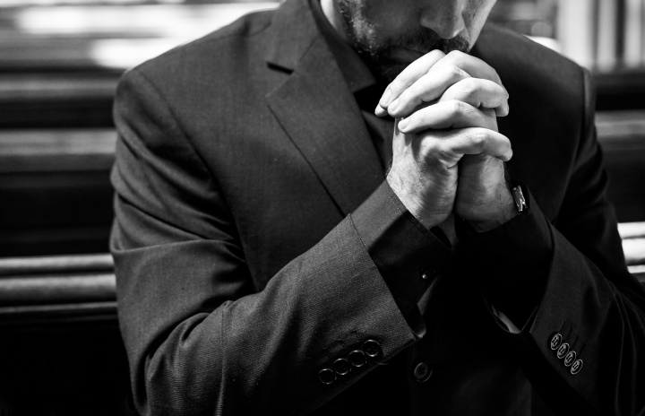 a man in a suit with hands folded in prayer